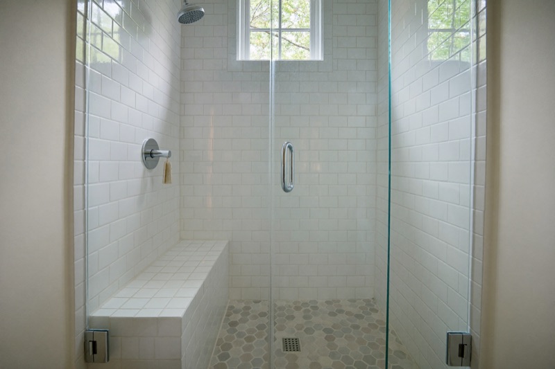 A frameless corner shower in white subway tile with a bench and hexagon mosaic floor.