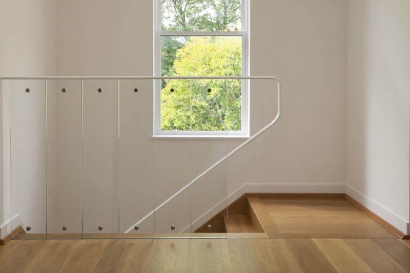 Frameless glass balustrade panels with standoff fixings at an oak stair landing.