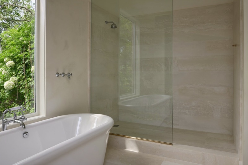 A single fixed frameless glass panel beside a freestanding soaking tub in a stone bathroom.