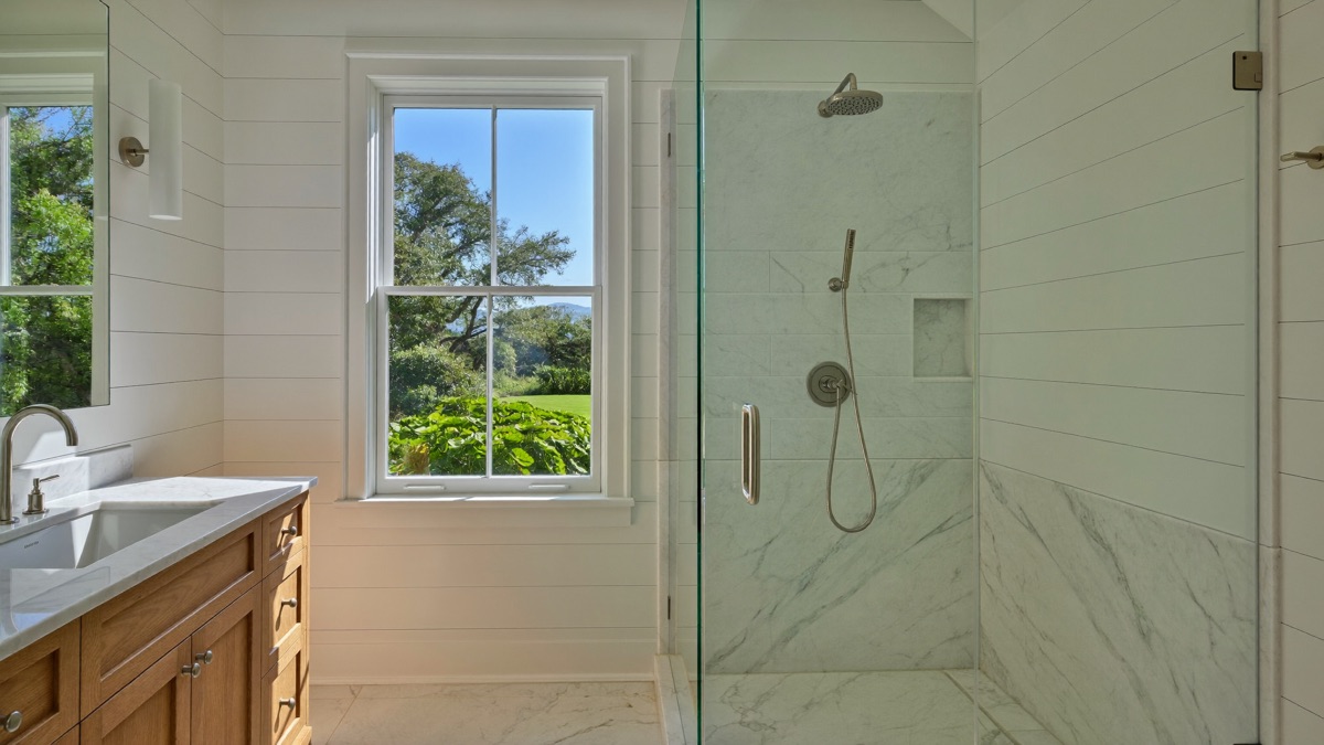 Frameless glass shower in marble with brushed nickel fittings, beside a white oak vanity. Illustrative.
