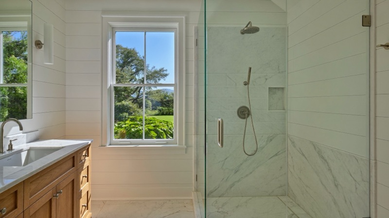 Frameless glass shower in marble with brushed nickel fittings beside a white oak vanity.